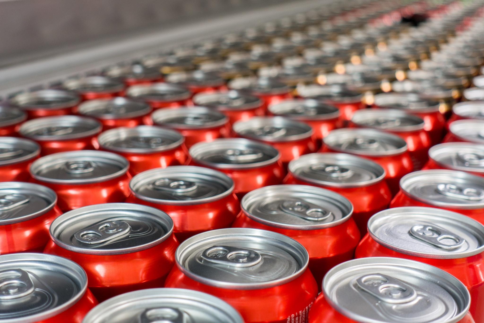 Rows of red aluminium drink cans with silver tops on a beverage packaging line