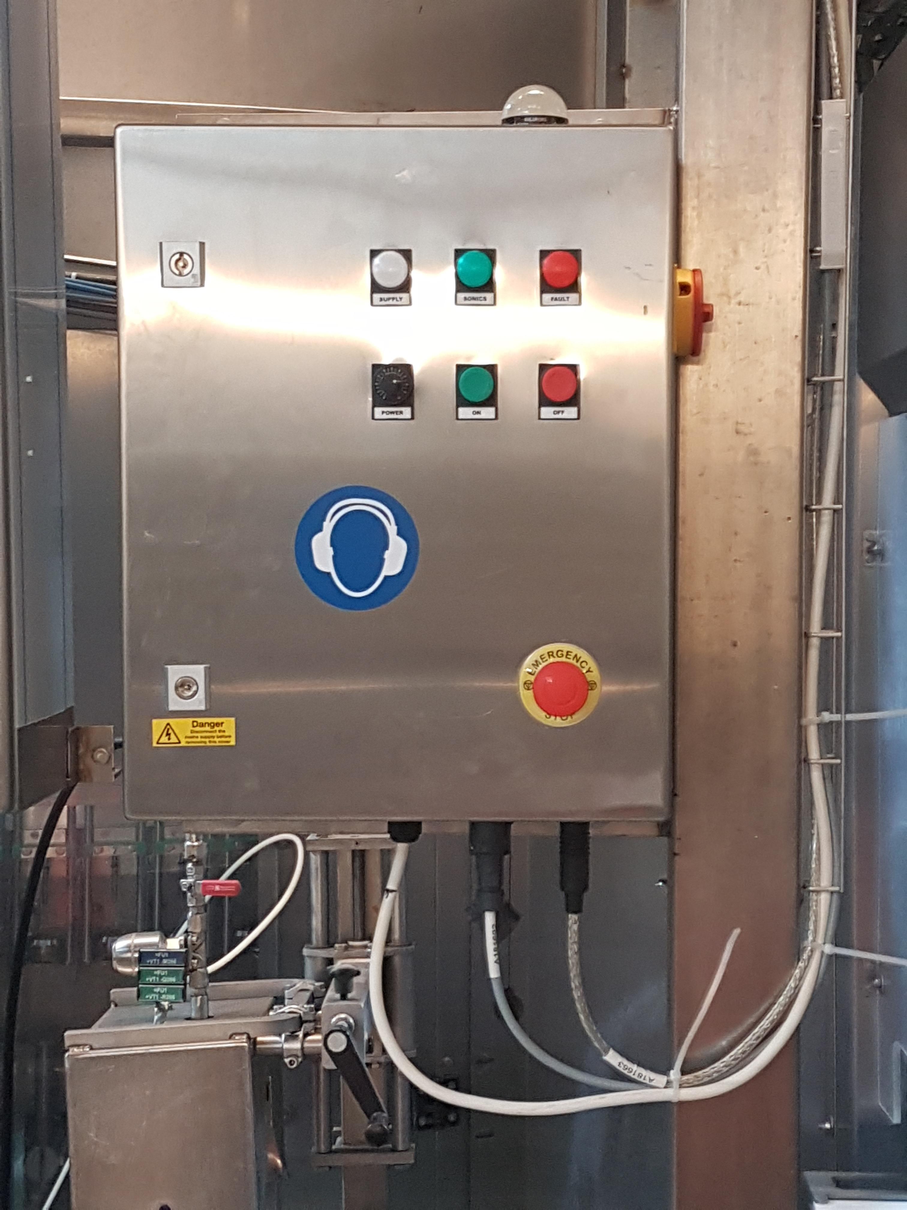 Stainless steel control cabinet with labelled push buttons, warning stickers, and a large emergency stop button, used for operating packaging machinery.