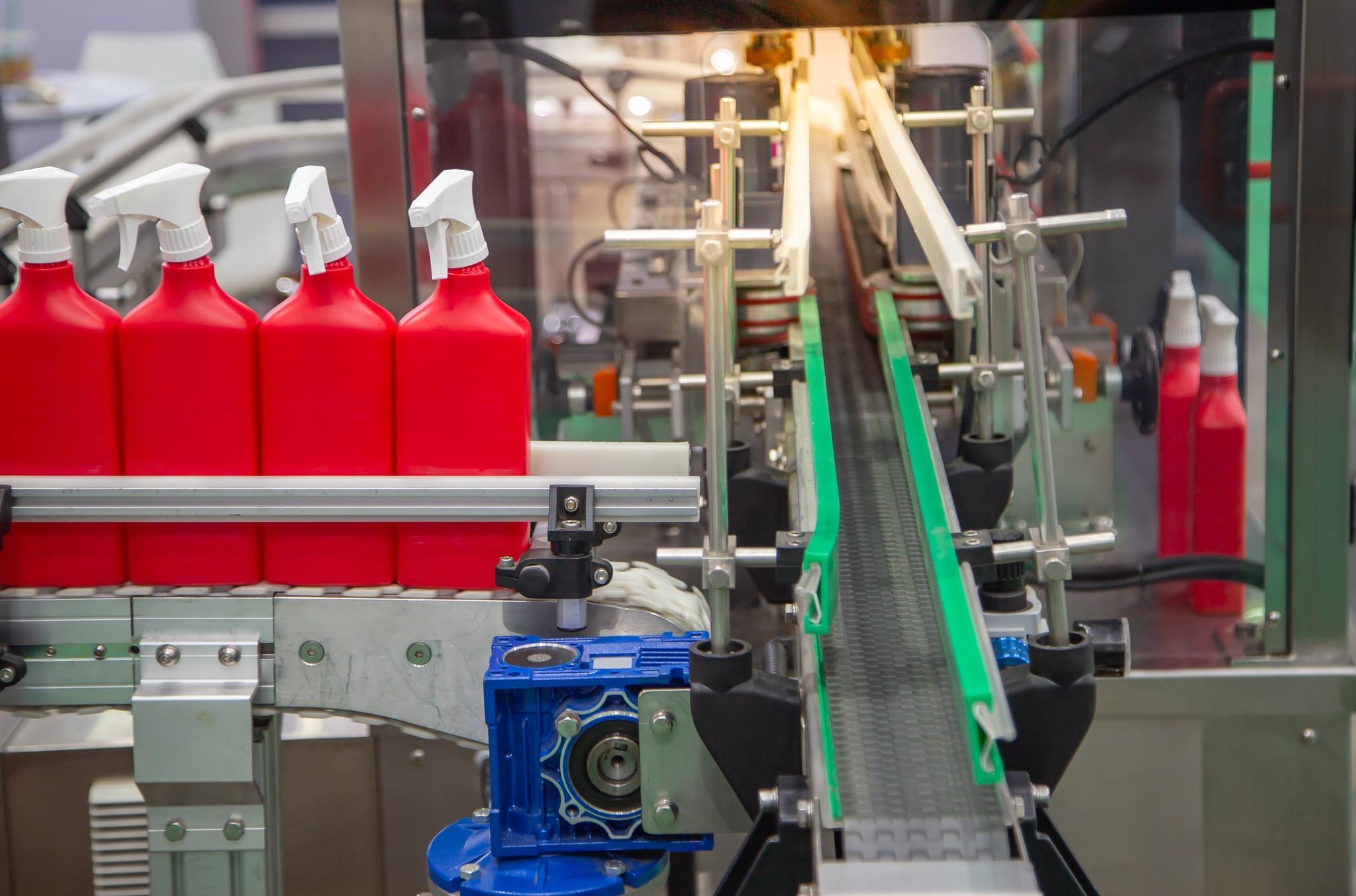 Red plastic spray bottles with white nozzles moving through an automated packaging line.