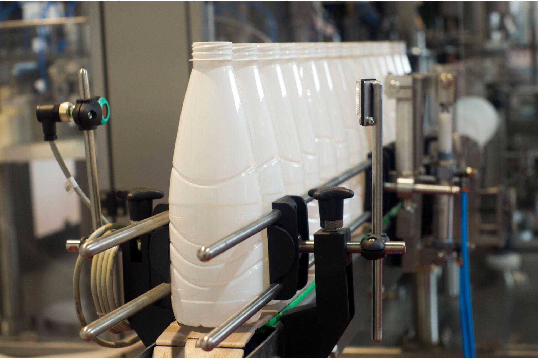White plastic dairy bottles aligned in a row on a packaging conveyor system